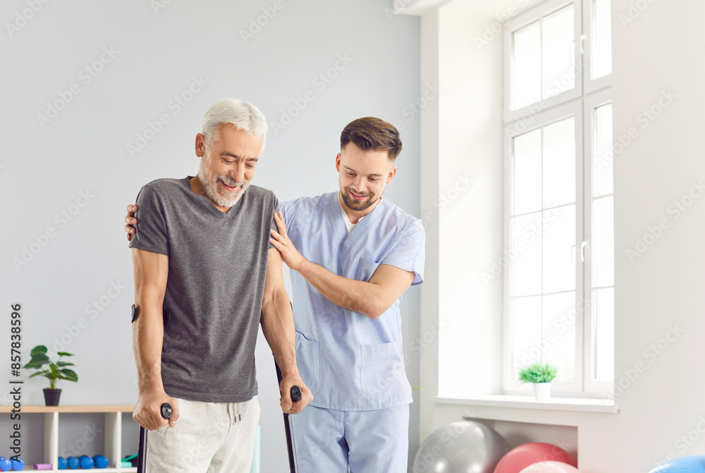 Obraz premium A happy elderly man walks with the help of a cane, a rehabilitation specialist is nearby. Patient support in a rehabilitation center. Restoring mobility after injury, joint disease