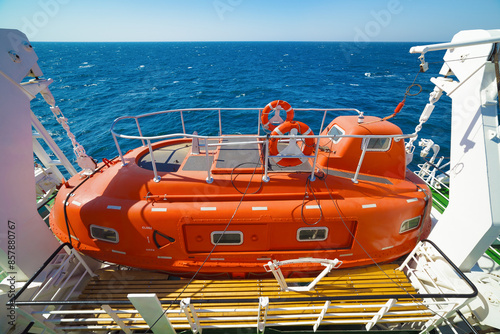 Orange lifeboat secured on deck of ship, set against blue sea and clear sky
