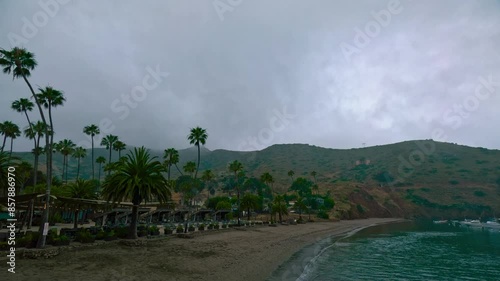 Tilt shot of small bay with sandy beach and palm trees on a rainy overcast day. A view of Santa Catalina island coastline and beach in the rain, with mountains in the background photo