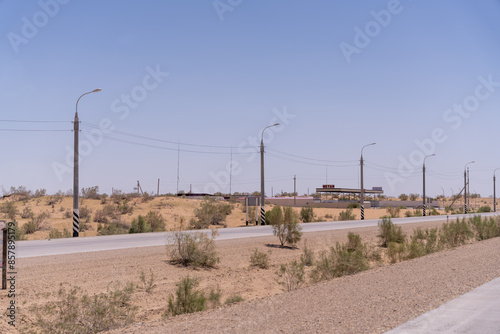 A road with a few trees and a few poles. The sky is blue