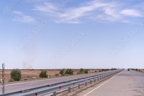 A long, empty road with a few trees in the distance. The sky is clear and blue