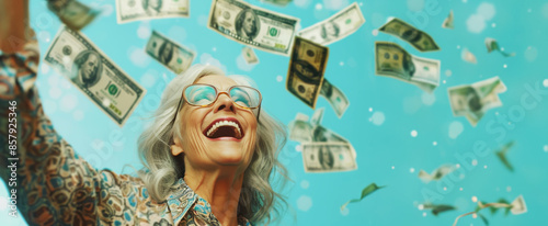 happy senior woman in her late sixties, with silver hair and glasses is smiling while throwing dollar bills into the air. Winning the lottery and raffle concept iwth copy space photo