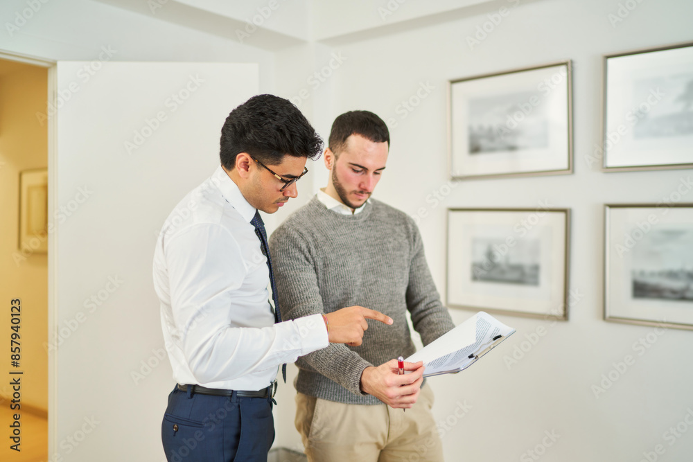 Two men are looking at a piece of paper, one pointing to it Two men are looking at a piece of paper, one pointing to it