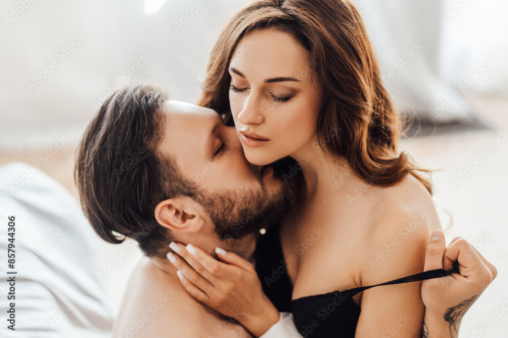 Fototapeta premium Sexy young undressed couple kissing with closed eyes sitting on the bed