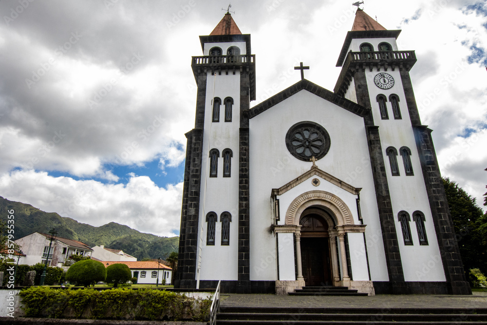 Fototapeta premium Ponta Delgada, White church with a clock tower under a bright sun and clear sky, with people walking nearby