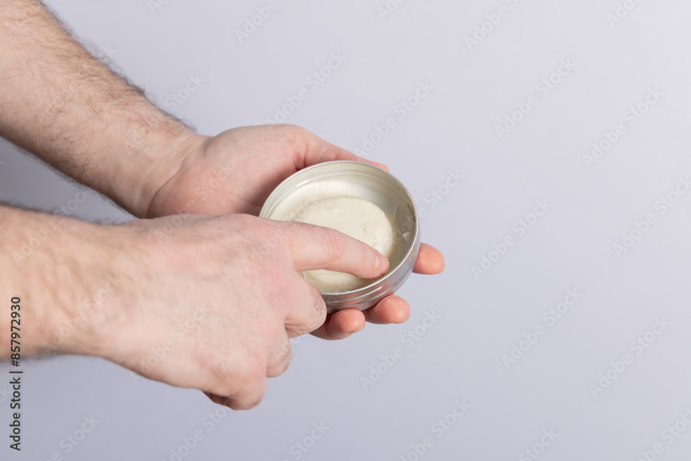 Man's hands grabbing with a finger hair pomade from a can isolated on grey background. Copy Space. Concept of cosmetics, male care and hair care Man's hands grabbing with a finger hair pomade from a can isolated on grey background. Copy Space. Concept of cosmetics, male care and hair care