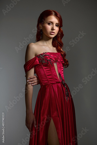 A young girl with exquisite makeup and good skin, a stylish hairstyle posing in the studio in a red dress on a dark background