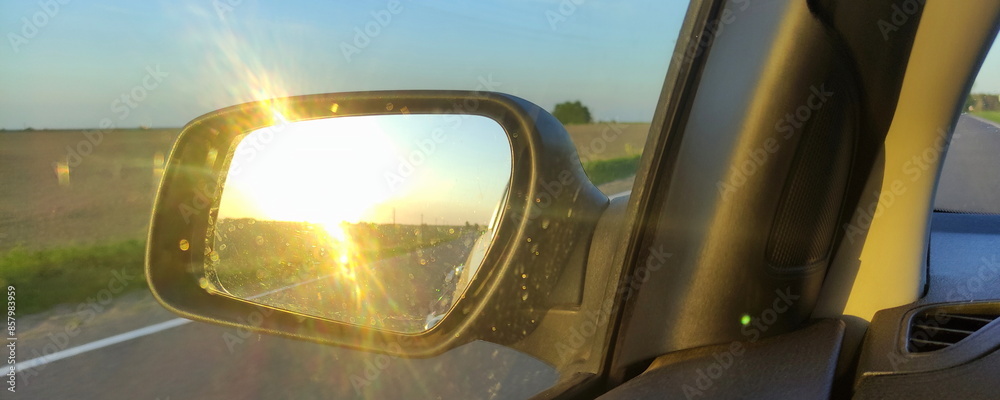 Car driving on a highway at evening. Sun in Sunset reflection in side mirror of vehicle