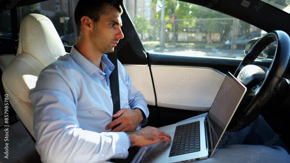 Handsome entrepreneur working on notebook while riding an autonomous self driving electric car at urban road. Male businessman typing text on laptop during riding on electrical vehicle with autopilot