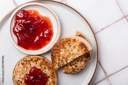 Hot Toasted Crumpets with piece of butter on a plate with strawberry jam. Perfect tasty breakfast popular in England, UK