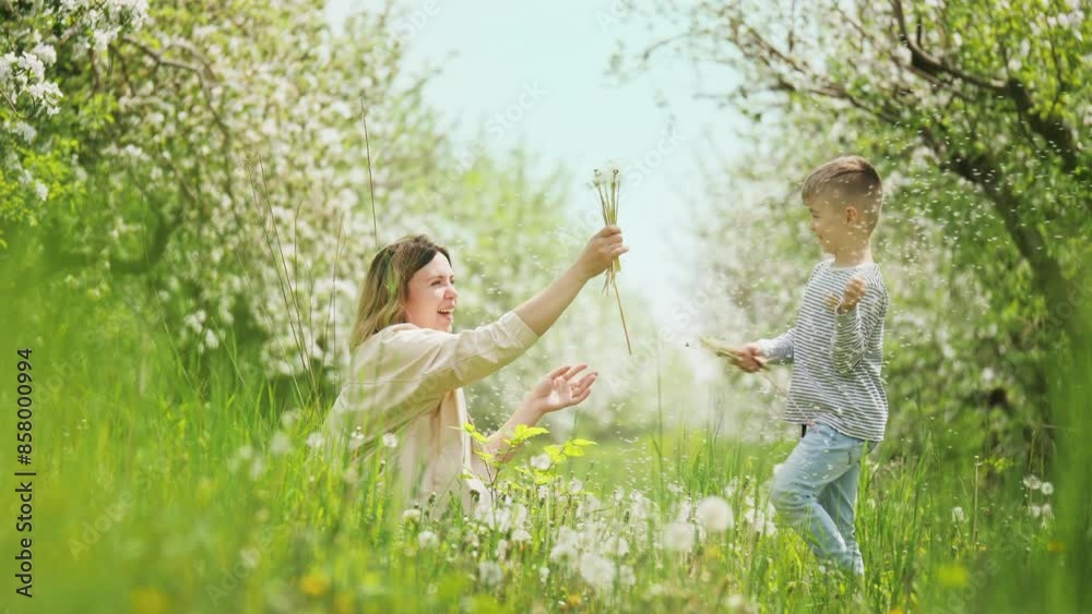 Smiling mother with happy little son play with dandelions in a blossoming apple orchard. Happy family weekend Smiling mother with happy little son play with dandelions in a blossoming apple orchard. Happy family weekend