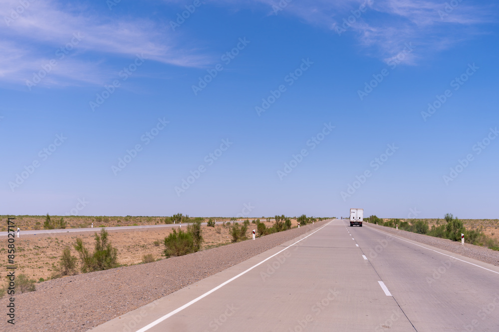 Fototapeta premium A road with a white truck driving down it. The sky is blue and there are no clouds