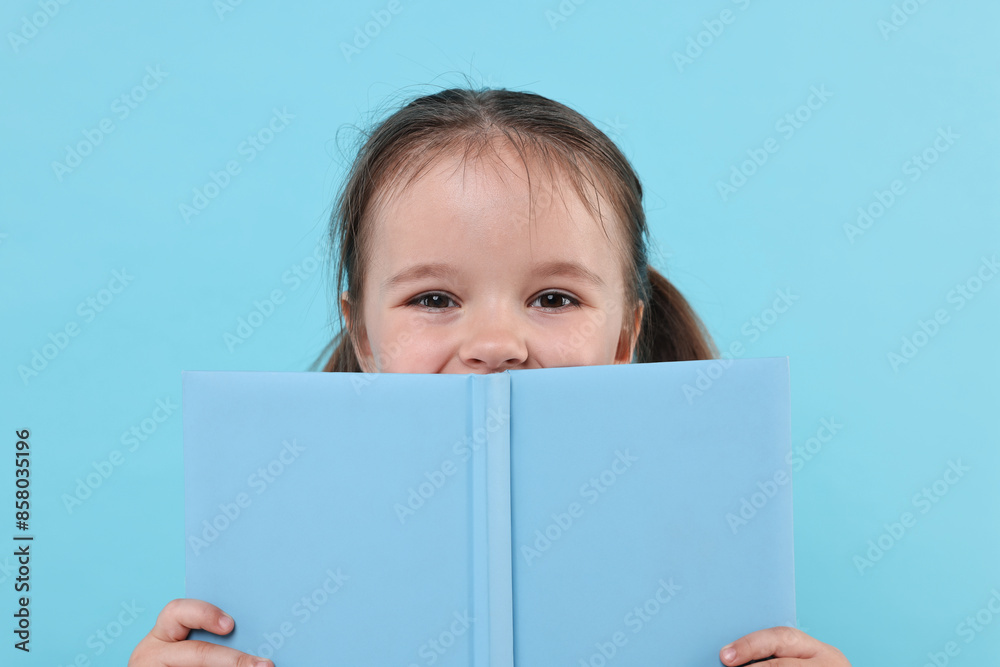 Cute little girl with open book on light blue background Cute little girl with open book on light blue background