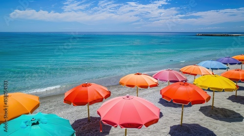 Array of beach umbrellas in vivid colors lining the sandy beach beside the calm sea © chanidapa