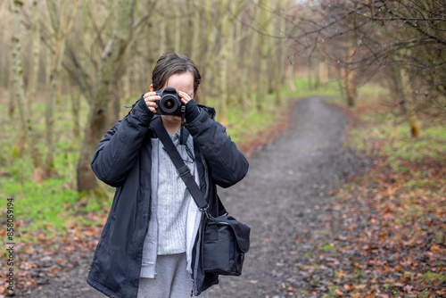 Young photographer teenage girl using DSLR camera outdoors in wood taking photos