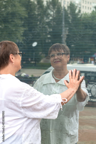 An elderly woman looks at her reflection in a shop window.