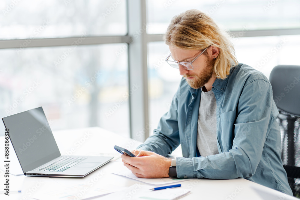 Young serious professional man, freelancer using smartphone in modern office Young serious professional man, freelancer using smartphone in modern office