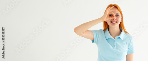 Obraz na płótnie Beautiful young woman wearing casual blue t-shirt doing ok gesture with hand smiling, eye looking through fingers with happy face. w salonie