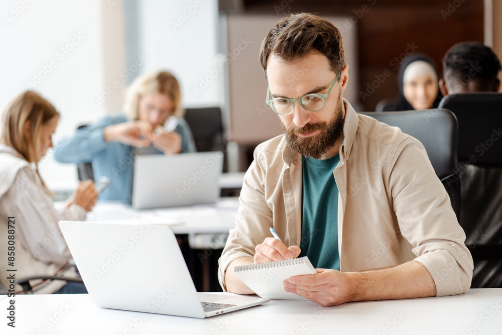 Focused male, manager, office worker taking notes during meeting, using laptop Focused male, manager, office worker taking notes during meeting, using laptop