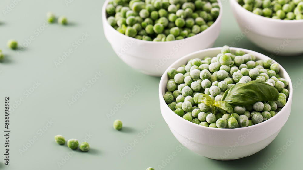 Three white bowls filled with frozen green peas on green background. Three white bowls filled with frozen green peas on green background.