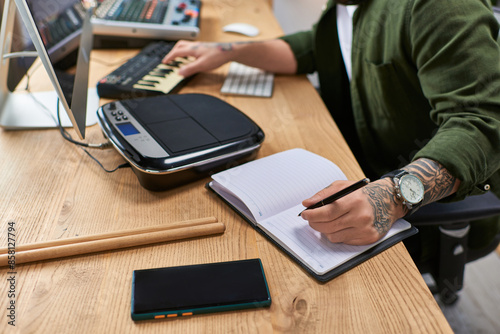 A handsome Asian man in casual attire works in his studio, writing in a notebook while surrounded by musical instruments. photo