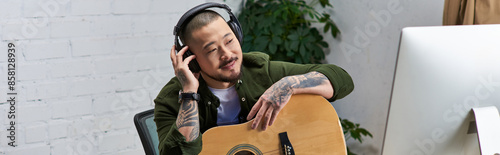 An Asian man in casual clothing plays guitar in his studio. photo