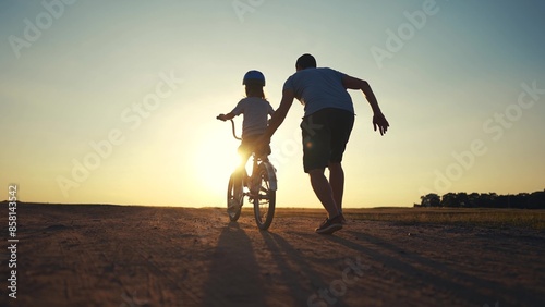 family play in the park. father teaching daughter to ride a bike. happy family kid dream concept. daughter learn to ride a bike silhouette. father supporting child riding sunset bike summer in park