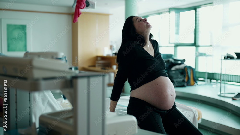 Pregnant woman having contractions seated by bedside struggling with pain during pre labor. third trimester pregnancy, maternal concept. person suffering