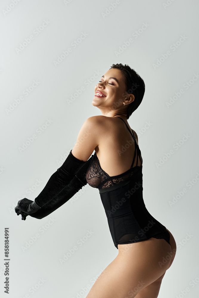 A woman in black lingerie smiles while posing in front of a white backdrop. A woman in black lingerie smiles while posing in front of a white backdrop.