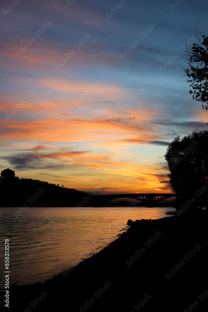 Fototapeta premium sunset in the city near the river. silhouettes of houses and bridge in the background
