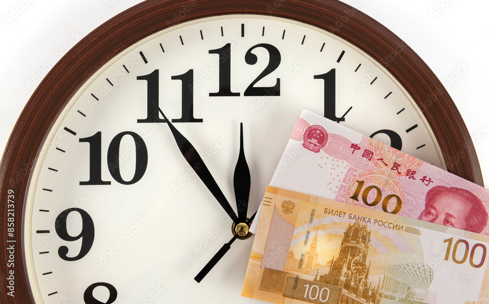 Banknotes in denominations of 100 Chinese yuan and 100 Russian rubles against the background of a clock Banknotes in denominations of 100 Chinese yuan and 100 Russian rubles against the background of a clock
