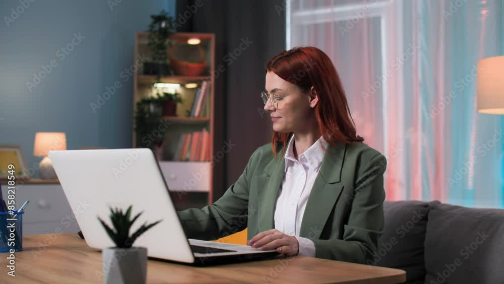 female entrepreneur working on laptop and writing in notebook sitting at table in evening at home female entrepreneur working on laptop and writing in notebook sitting at table in evening at home