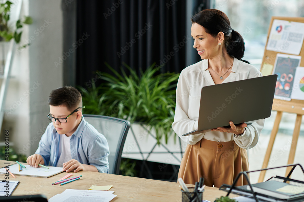 A mother works on her laptop in her office, while her son with Down syndrome sits at a table drawing. A mother works on her laptop in her office, while her son with Down syndrome sits at a table drawing.
