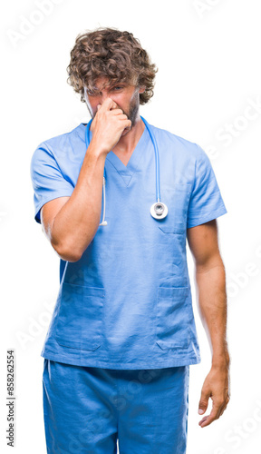 Handsome hispanic surgeon doctor man over isolated background smelling something stinky and disgusting, intolerable smell, holding breath with fingers on nose. Bad smells concept.