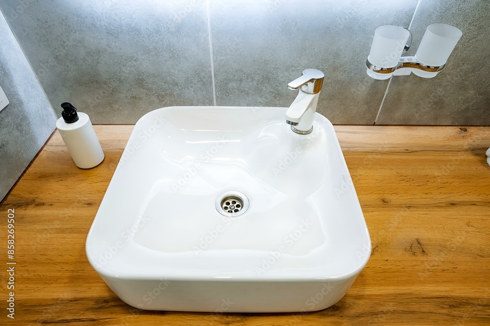 Fototapeta premium The white sink pairs beautifully with the wooden bathroom counter, creating a cohesive look that enhances the rooms appeal aesthetically and blends seamlessly with the surroundings
