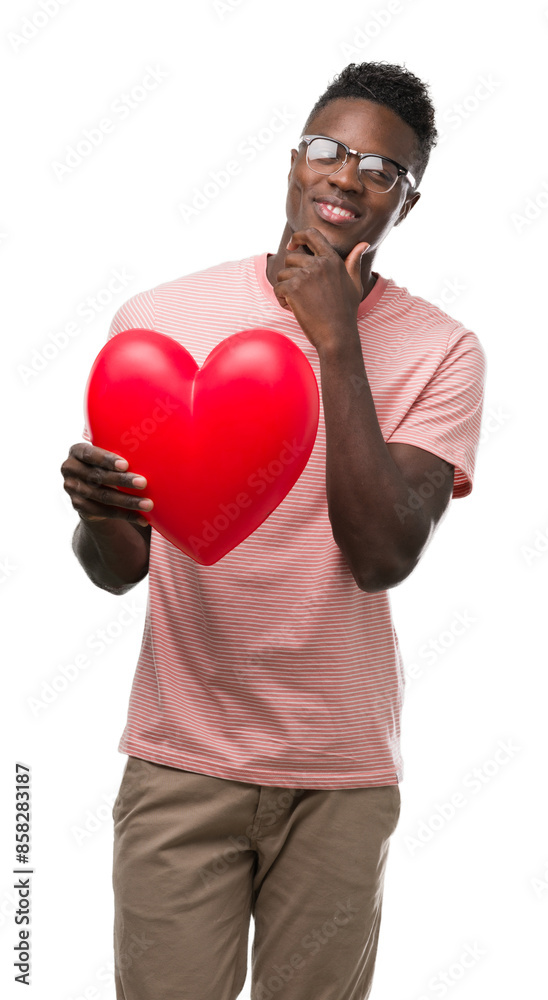 Young african american man holding red heart serious face thinking about question, very confused idea Young african american man holding red heart serious face thinking about question, very confused idea