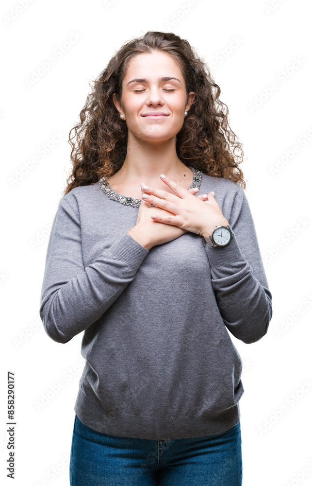 Beautiful brunette curly hair young girl wearing a sweater over isolated background smiling with hands on chest with closed eyes and grateful gesture on face. Health concept. Beautiful brunette curly hair young girl wearing a sweater over isolated background smiling with hands on chest with closed eyes and grateful gesture on face. Health concept.