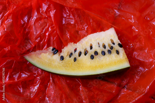 Yellow watermelon slice with many seeds. Watermelon in red plastic background photo