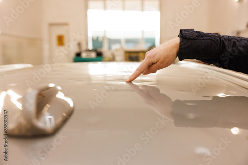 The person is pointing at the car hood with their index finger to show car dent removal problem of the car roof