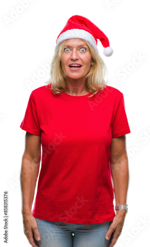 Middle age blonde woman wearing christmas hat over isolated background afraid and shocked with surprise expression, fear and excited face.