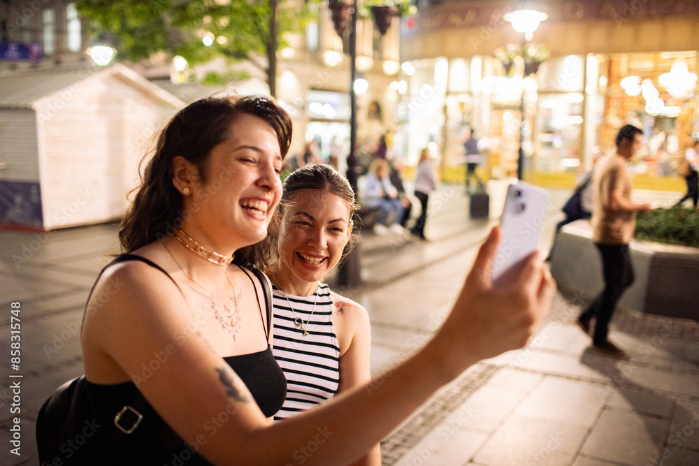 Lesbian couple laughing while using smartphone in city Lesbian couple laughing while using smartphone in city