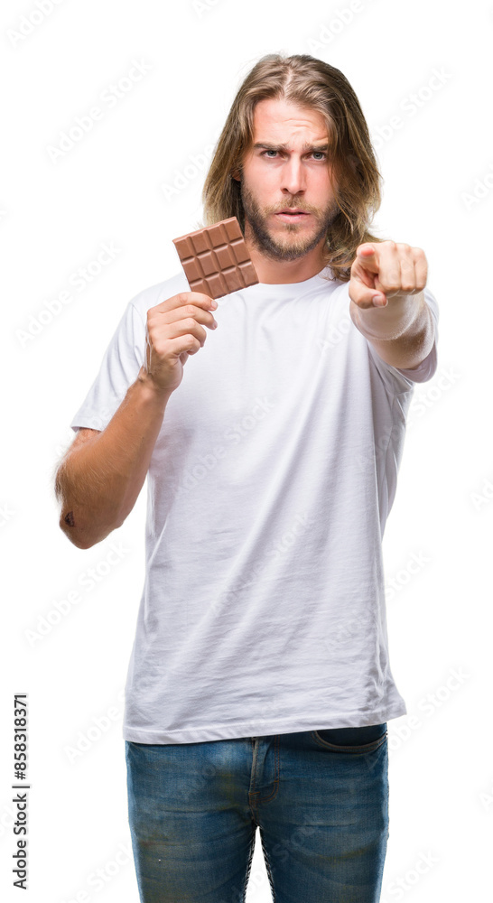 Young handsome man with long hair eating chocolate bar over isolated background pointing with finger to the camera and to you, hand sign, positive and confident gesture from the front Young handsome man with long hair eating chocolate bar over isolated background pointing with finger to the camera and to you, hand sign, positive and confident gesture from the front