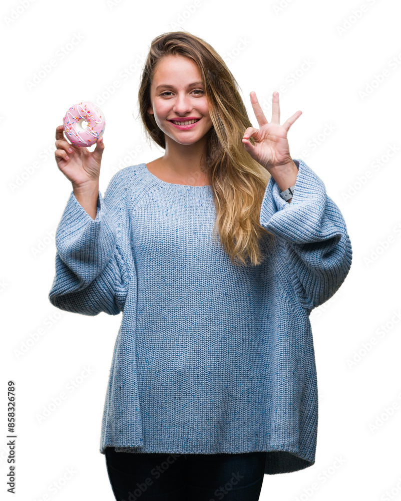 Obraz premium Young beautiful blonde woman eating sweet donut over isolated background doing ok sign with fingers, excellent symbol