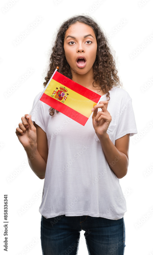 Young hispanic woman holding flag of Spain scared in shock with a surprise face, afraid and excited with fear expression Young hispanic woman holding flag of Spain scared in shock with a surprise face, afraid and excited with fear expression