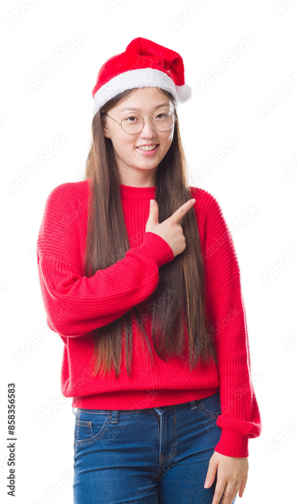 Young Chinese woman over isolated background wearing christmas hat cheerful with a smile of face pointing with hand and finger up to the side with happy and natural expression on face. Young Chinese woman over isolated background wearing christmas hat cheerful with a smile of face pointing with hand and finger up to the side with happy and natural expression on face.