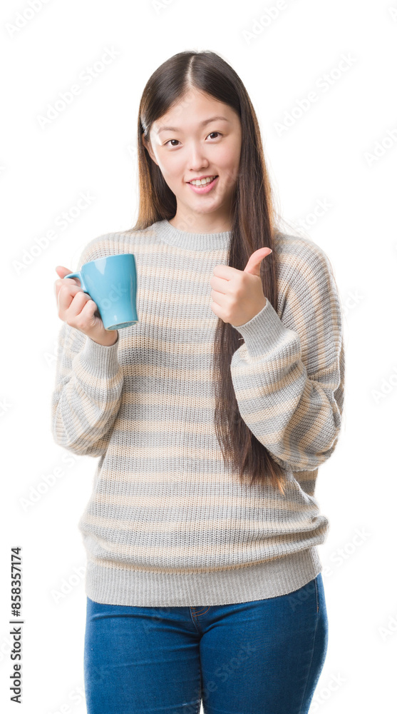 Young Chinese woman over isolated background driking cup of coffee happy with big smile doing ok sign, thumb up with fingers, excellent sign