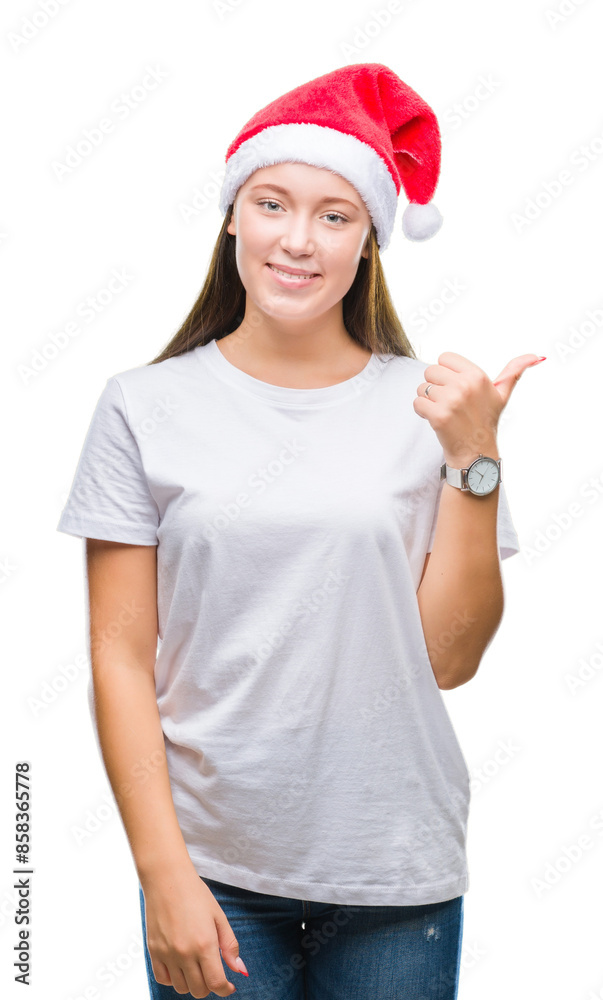 Young beautiful caucasian woman wearing christmas hat over isolated background smiling with happy face looking and pointing to the side with thumb up. Young beautiful caucasian woman wearing christmas hat over isolated background smiling with happy face looking and pointing to the side with thumb up.