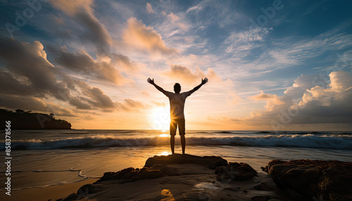 Man standing on a rocky outcropping with his arms spread wide, looking out towards the ocean as the sun sets.
