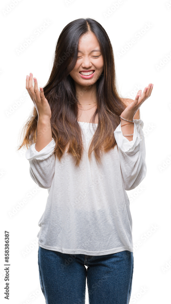 Young asian woman over isolated background celebrating mad and crazy for success with arms raised and closed eyes screaming excited. Winner concept Young asian woman over isolated background celebrating mad and crazy for success with arms raised and closed eyes screaming excited. Winner concept