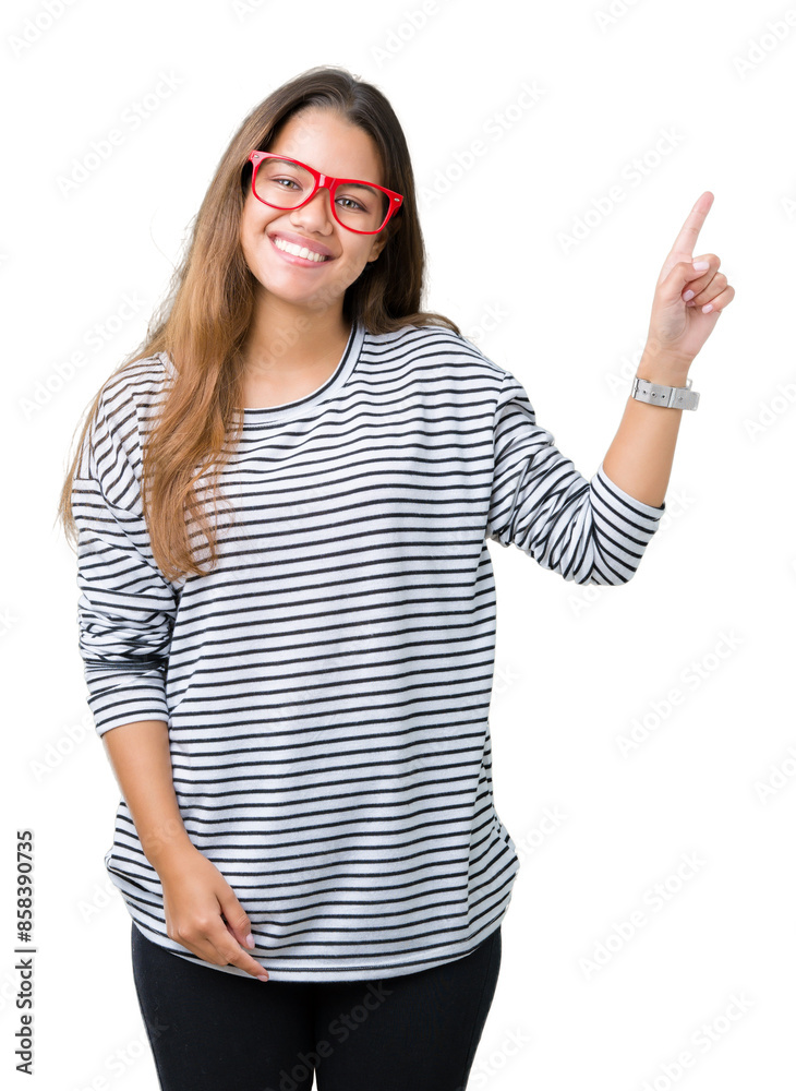 Young beautiful brunette woman wearing stripes sweater and red glasses over isolated background with a big smile on face, pointing with hand and finger to the side looking at the camera. Young beautiful brunette woman wearing stripes sweater and red glasses over isolated background with a big smile on face, pointing with hand and finger to the side looking at the camera.